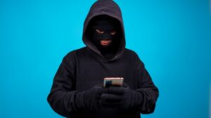 A criminal in black outfit with face covered messaging on a phone